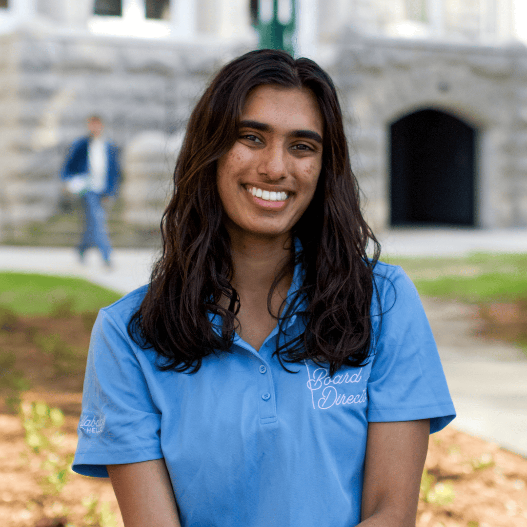 Smiling young woman in a blue polo shirt with 'Board of Directors' logo outside a stone building.