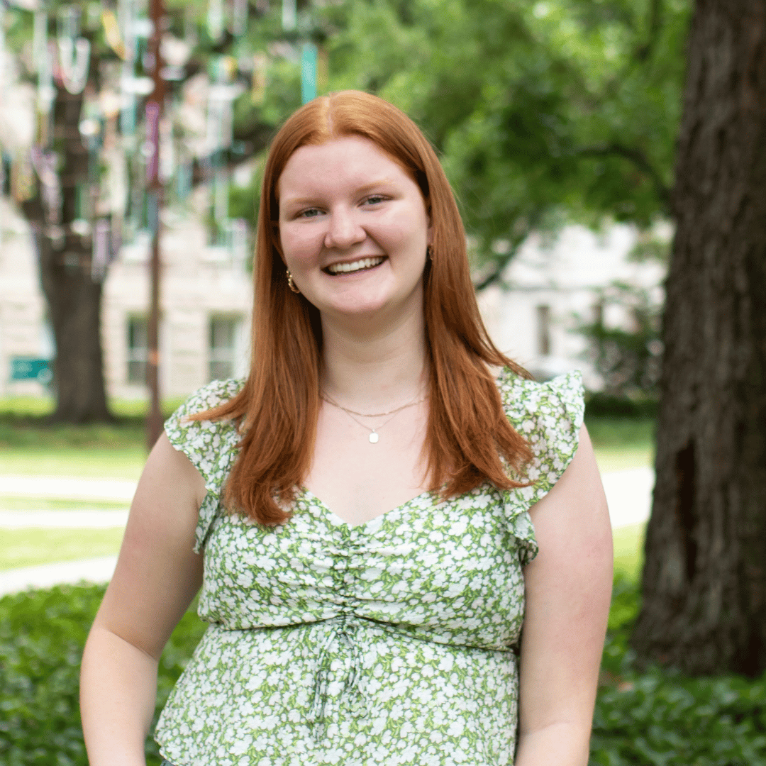 Smiling young woman with red hair in a green floral top outdoors.
