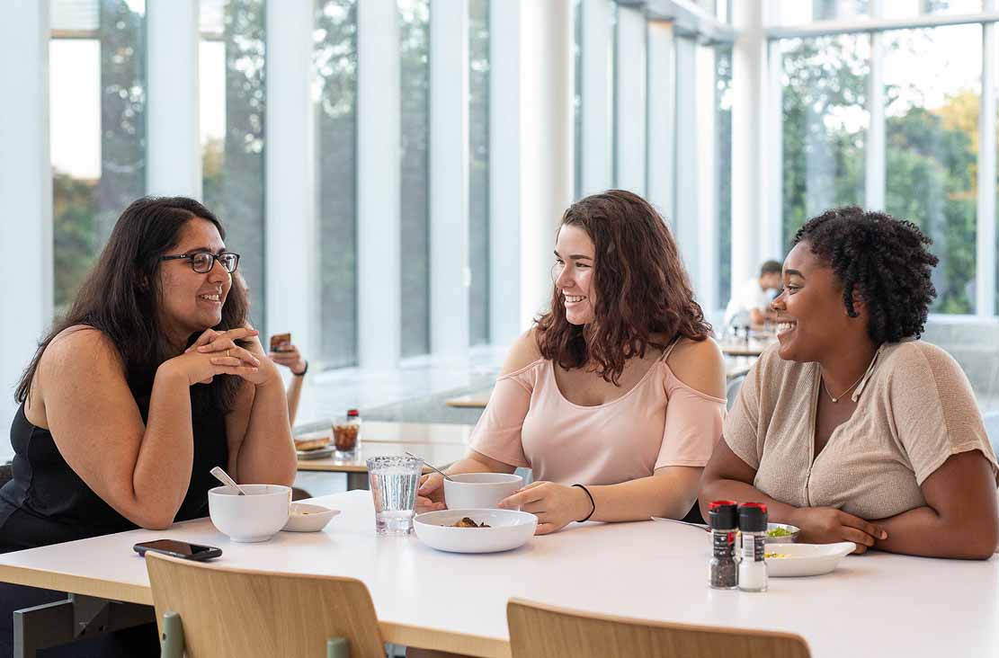 Female students gather around a table in the Commons dining hall